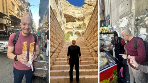Imad Alarnab Three photos side-by-side across the screen, showing Imad Alarnab during his visit to Syria. On the left, he is shown standing in a busy street with traffic behind him, holding two wraps and looking at the camera, smiling. In the middle, he is standing at the bottom of a set of stone steps at a historical site. On the right, he is standing in front of a kiosk at a street food stall, talking to a man who is preparing some food.
