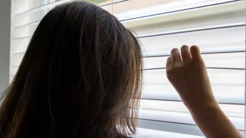 A women peering through her blinds looking out of a window.