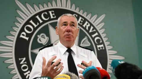 Getty Images John Boutcher in white shirt and black tie, stood against PSNI crew