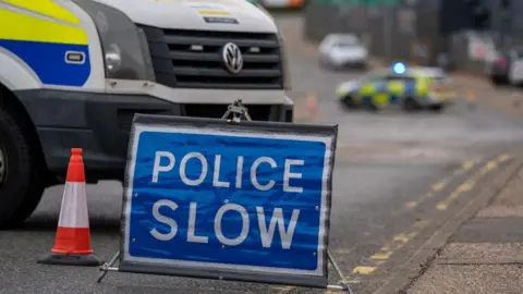 A blue Police slow down road sign in front a white police van on the road 