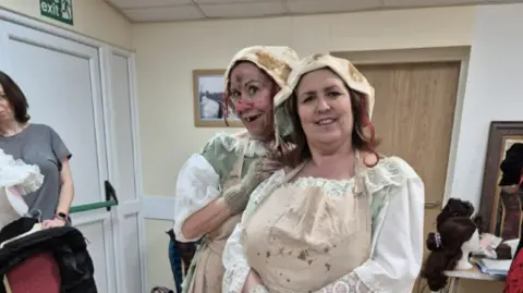 Judy Shone Two women in dirty white dresses in a room with beige walls and white doors