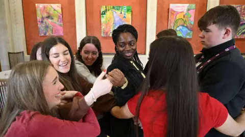 Michael Cooper A group of young people stand in a circle holding hands. 