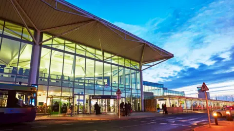 Getty Images A night-time shot of Bristol Airport's terminal. Silhouettes of passengers are visible in the background. The terminal is brightly lit and the sky is dark blue  