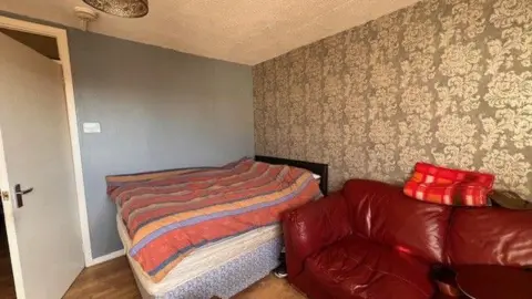 Gary Bennett A bed and a sofa inside a flat, the interior door is open.