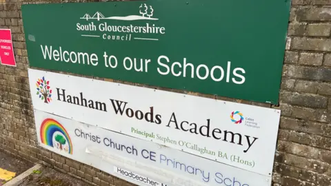 A school sign on a brick wall welcomes people to Hanham Woods Academy