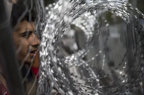 Getty Images A refugee looks through the fence on the Serbia-Hungary border, September 2015