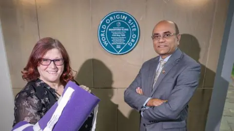 University of Bradford Dr Kirsten Riches-Suman, Associate Professor of Biomedical Science at the University of Bradford, wearing the Bradford Sling, and Professor Ajay L Mahajan standing in front of the plaque