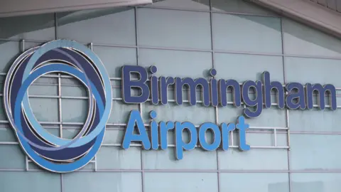 A close-up photo showing the windows of a building, with a sign across the windows that says "Birmingham Airport" in blue letters along with a logo made up of blue circles.