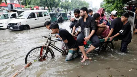 Several people push a heavily laded tricycle through floodwaters in Dhaka