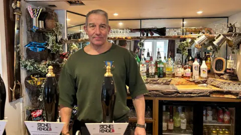 The Plume of Feathers pub landlord Colin Nufer looking at the camera behind the pub's counter