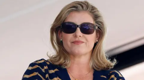 Getty Images Penny Mordaunt wearing sunglasses and a striped top. She has shoulder length blonde hair.