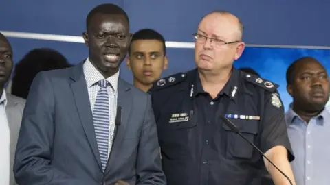EPA Kot Monoah, a leader in the local South Sudanese community, speaks to the media alongside Victoria's police chief Graham Ashton during a press conference on Wednesday