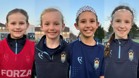 (Left to right) Harper, Eadie, Grace and Alba. A composite image of all four of the girls smiling at the camera. They all have their hair tied back, the two girls on the right are also wearing headbands. Harper wears a rest sports vest over her top, while the other three girls wear navy sports jumpers with a crest on. 