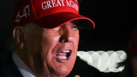 US President Donald Trump wearing red cap with 45-47 seen on the side and GREAT AGAIN seen on the front