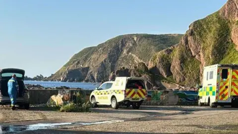 An ambulance and a coastguard rescue vehicle parked close to the rocky shore at Gardenstown in Aberdeenshire