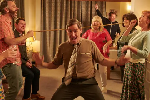 BBC/Toffee International Ltd/Tom Jackson Rob Brydon pictured doing the limbo on set at Pam & Mick's house in Essex.