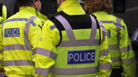 BBC The back of police officers in bright yellow police jackets