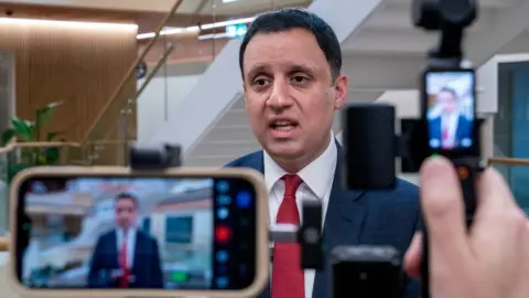 PA Media Anas Sarwar, who has short black hair, speaks to the media while wearing a business suit 
