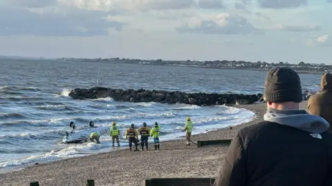 Gary Firth Fire crews gather around the upturned aircraft on the shore