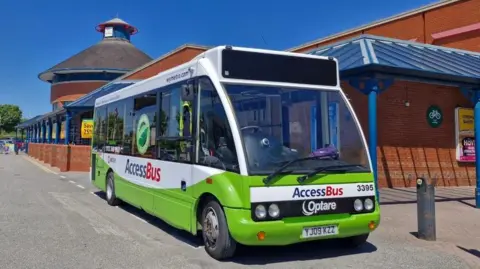 A white and green bus which has writing on it which says 'AccessBus'