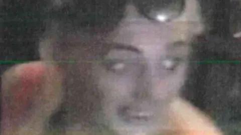 Merseyside Police A blurry CCTV still showing a woman with blonde hair and a pink vest-top, with sunglasses perched on her head.