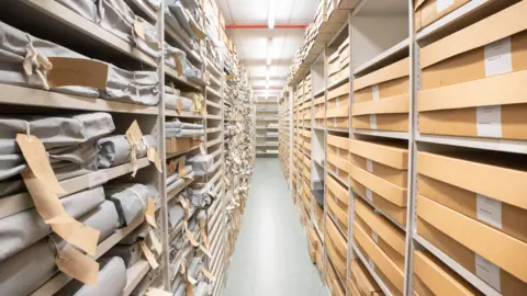 Inside of archive building showing rows of metal shelves stacked with matching boxes and bags