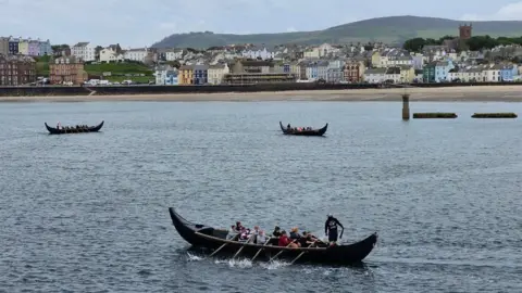VIKING LONGBOAT RACES Three teams out in Peel Bay practicing for the event. Peel Beach and promenade are in the background.
