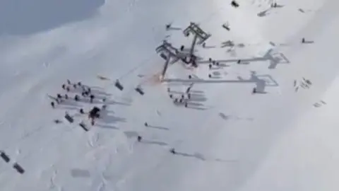 Guardia Civil An aerial shot of a collapsed ski lift. A group of people can be seen gathered on the snow in the lower third of the shot.