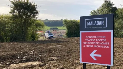 Martin Heath/BBC Muddy construction site with Malabar sign in foreground