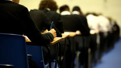 School pupils in dark uniforms doing an exam in an exam hall at individual tables 