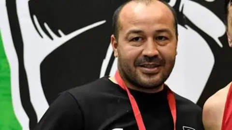 Getty Images Tulkin Kilichev poses for the camera with another boxer. Tulkin Kilichev wears a black sport top