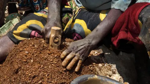 Getty Images A woman breaks stones containing cassiterite ore at a mine in the Szibira district, Democratic Republic of Congo, in April 2009