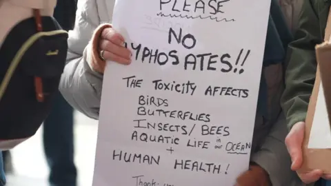 A sign which says 'please no glyphosate the toxicity affects birds, butterflies, insects, bees, aquatic life in our ocean and human health'.