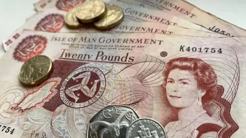 BBC Brown and red Manx £20 notes fanned out with several Manx coins on top of them.