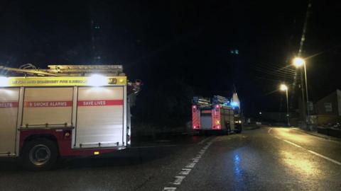 Two fire engines parked by the side of a road, at night.