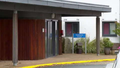 A picture of the entrance to Oberlands. It is a wooden centre with a blue sign outside of it.