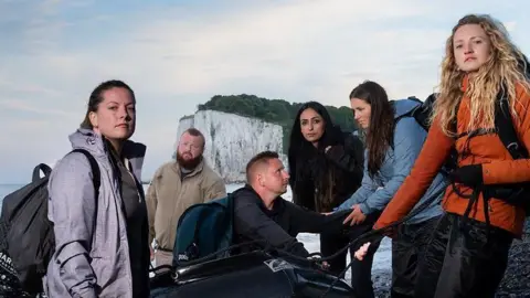 Channel 4 Six people - four women and two men - around a small boat on a Dover beach, for a promotional photo for Channel 4's Go Back To Where You Came From 