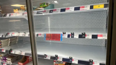 A chiller cabinet at the Co-Op in Loose Road, Maidstone, is left half empty with signs apologising for items not being in stock