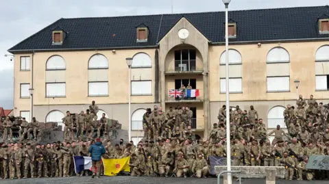 A group shot of soldiers in front of a house with a French flag and a UK flag in the middle
