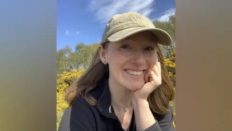 Photograph of Lily Sparrow. She has shoulder length brown hair and is wearing a baseball cap