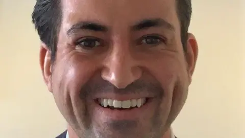 University of Sheffield A close up shot of a man with straight white teeth, a very short goatee, and dark-brown eyes, eyebrows and hair.