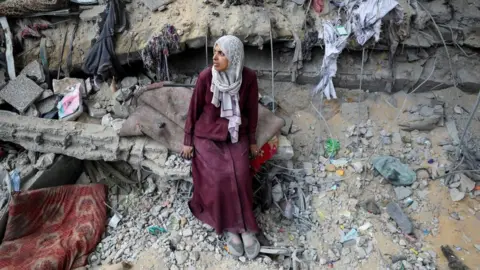 A Palestinian woman looks to her right, sitting amidst the rubble of a very badly damaged building in Gaza City