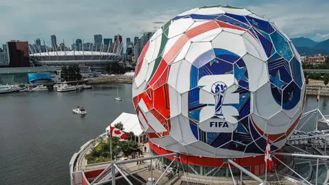 An aerial shot of circular building that has been covered in Adidas decals and posters to make it look like the World Cup match ball. In the background you can see BC Place, one of the World Cup venues.