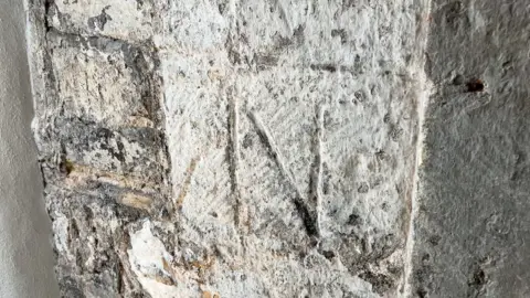 Kit Taylor/BBC A stone gate wall with the initials A and N carved in.