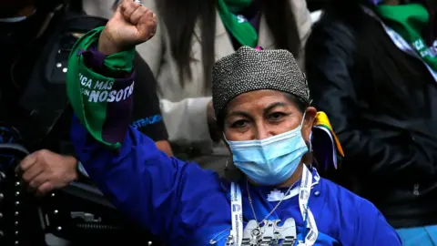 Getty Images Elisa Loncón after being elected, wearing a face mask due to Covid regulations, dressed with traditional Mapuche clothes and silver jewellery, and holding her right fist in the air as a symbol of pride for her people.