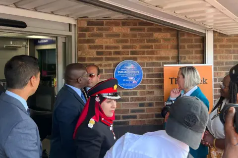 Lauren Carter/BBC People look at a circular blue plaque commemorating the 75th anniversary of the first Windrush arrivals