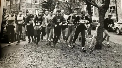 Northumberland Gazette A black and white photograph of lots of men wearing bibs and just beginning to run 