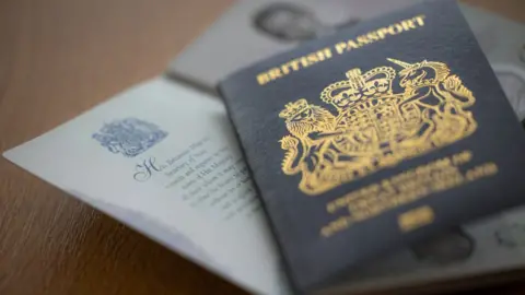 A British passport laid on a table on top of another open passport. The cover is dark blue and gold.