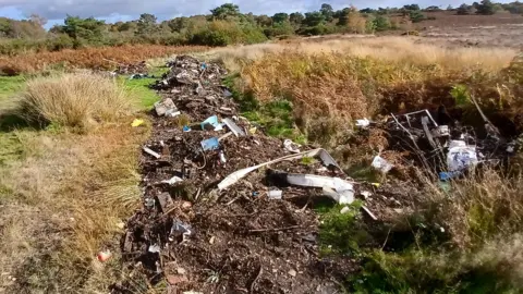 An open area of heathland with a wide row of mashed up rubbish strewn in a long line