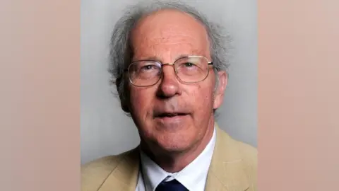 Middlesbrough Council A head-and-shoulders portrait of councillor David Branson. He has grey thinning hair and wears glasses with a metal rim. He wears a beige jacket over a white shirt and blue tie.